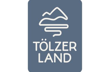 The logo is divided horizontally. At the top, the blue symbol on a white background shows mountains and the Isar. Below this, the words Tölzer Land in orange. Below in white lettering on a blue background: Bavaria's picture book country