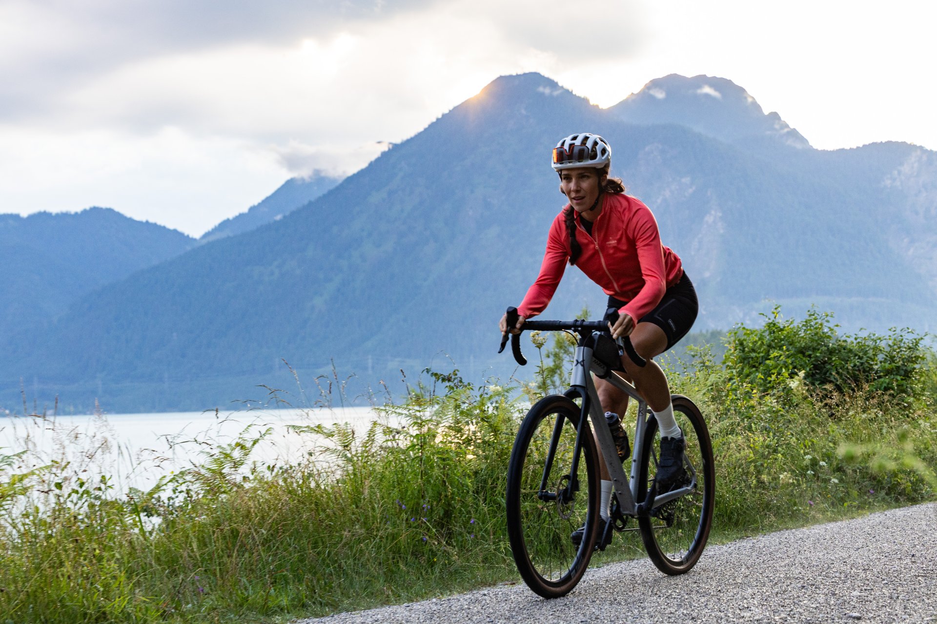 A cyclist rides along a tarred road by the Walchensee. Mountain peaks can be seen in the background.