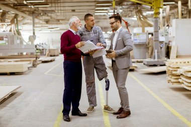 three men in a production hall in wood processing, man with prosthetic leg