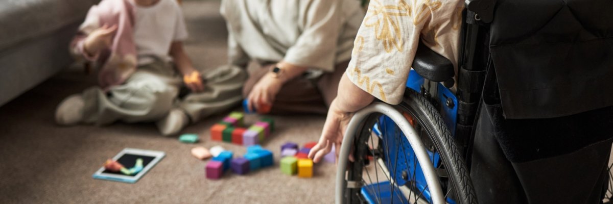 Child in a wheelchair A youngster in a wheelchair sits on the carpet while another child plays on the floor with an adult.