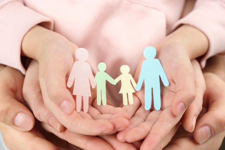 Several hands are holding a large number of paper figures that symbolically represent a family.