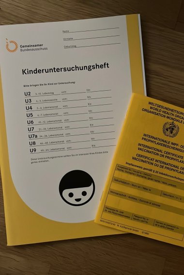Photograph of an examination booklet for the preventive medical check-up and the vaccination card. Both booklets are yellow.