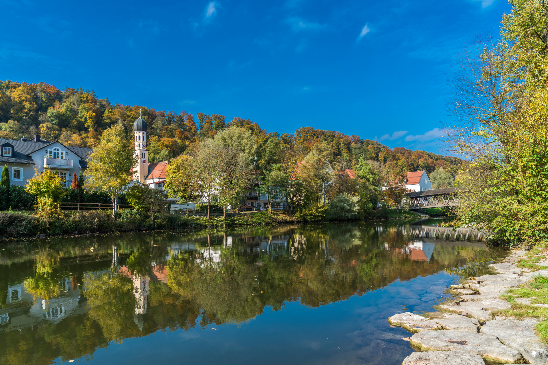 The old town of Wolfratshausen reflected in the Loisach in fall Photograph from the banks of the Loisach across the river with a view of the church and wooden bridge.