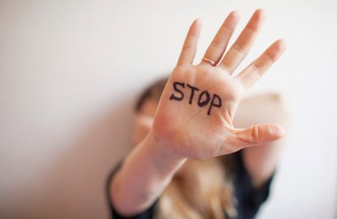 Woman shows palm with the inscription on the palm "Stop" Im Hintergrund verschwommen eine Frau, die sich die linke Hand schützend vor das Gesicht hält. Im Vordergrund die rechte Hand einer Frau mit Ring, Finger gespreizt. Im Handteller der Schriftzug STOP in schwarzen Buchstaben.