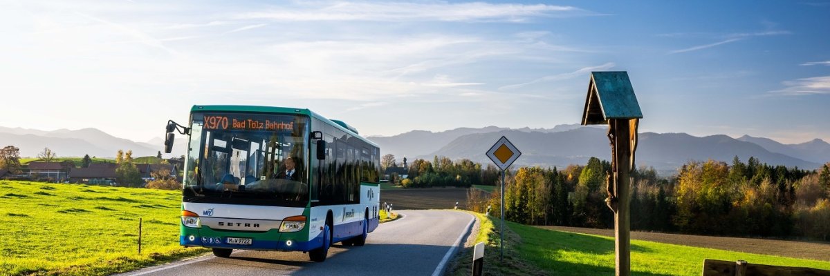 Bus vor Bergkulisse Ein Bus fährt vor der Bergkulisse an grünen Wiesen vorbei.