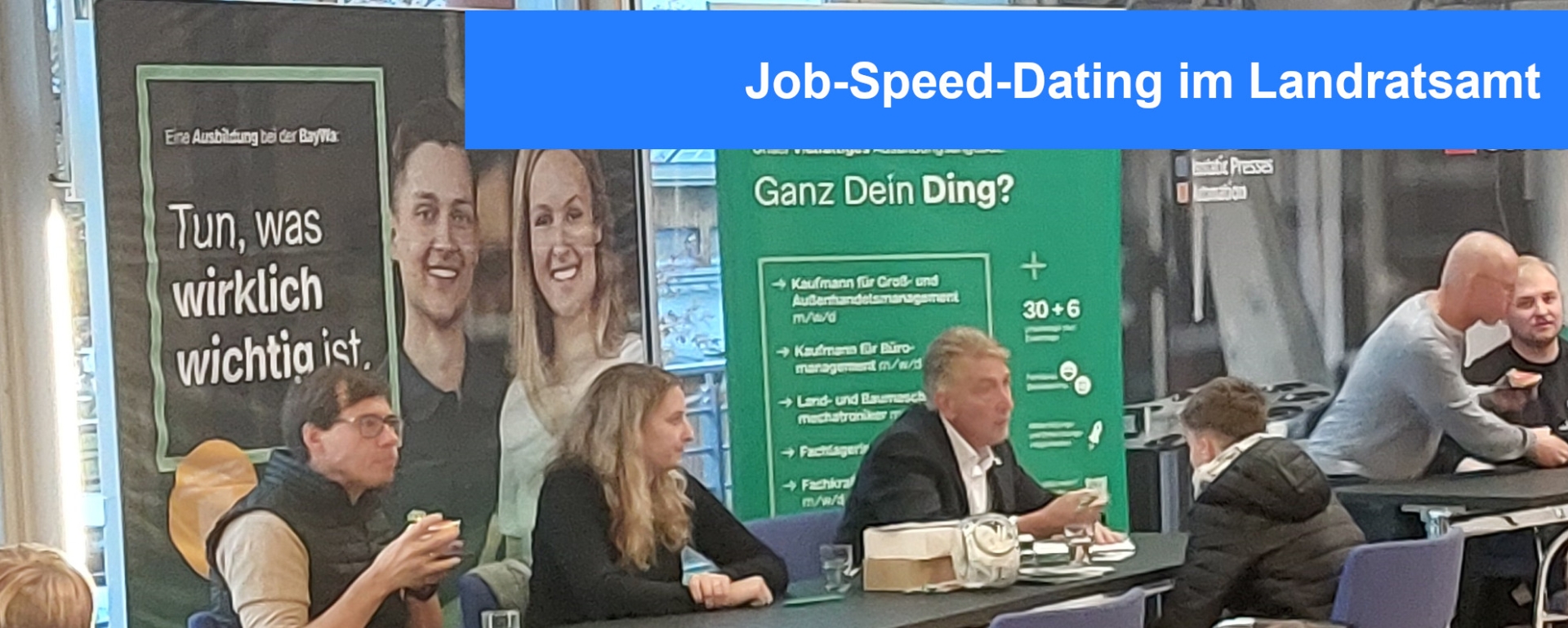 Job Speed Dating im Landratsamt Tische stehen vor Aufstellwänden, an denen Firmenplakate hängen. Darüber steht der Titel Job Speed Dating im Landratsamt