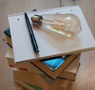 Bücherstapel darauf liegt eine Glühbirne und ein Stift