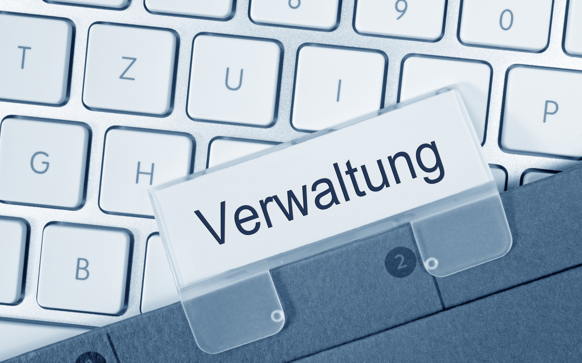 Verwaltung Darstellung einer Computertastatur darauf liegt ein Aktenhefter mit dem Label "Verwaltung".