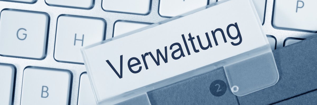 Verwaltung Darstellung einer Computertastatur darauf liegt ein Aktenhefter mit dem Label "Verwaltung".